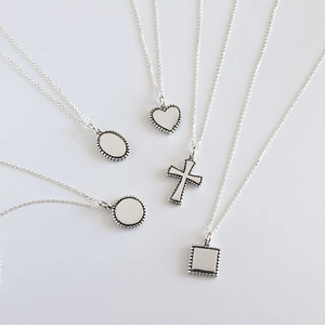 Flat lay of five minimalist S925 silver necklaces with various geometric pendants on white
