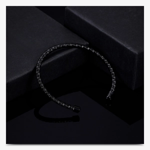 Macro detail of black braided cable cuff bracelet on matte black gift box with reflections