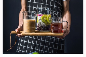 Three heat-resistant glass measuring cups with scales on a wooden tray held by a person