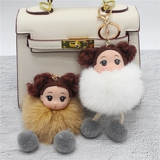 Detail showing plush fur ball charms with doll heads on a white handbag with gold clips
