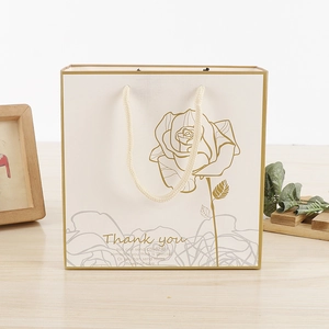 Detail of white gift bag featuring golden rose pattern and matching gold handle ropes