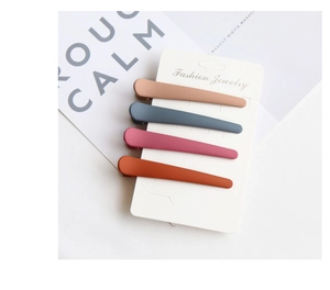 Close-up of four matte-finished duckbill hair clips in brown, blue, rose, and red colors
