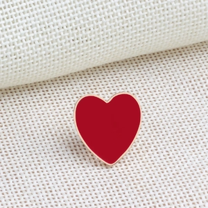 Close-up of a red enamel heart brooch with gold metal edges on beige woven fabric