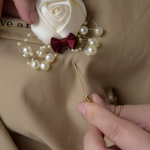 Detail of cream silk rose boutonniere with burgundy bow and pearls on a trench coat