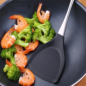 Silicone spatula with stainless steel handle cooking broccoli and shrimp in a black wok