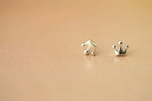 Macro shot of silver crown stud earrings with polished finish on a warm brown base
