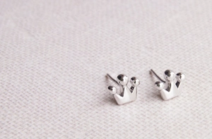 Detailed view of polished silver crown stud earrings on textured pink fabric