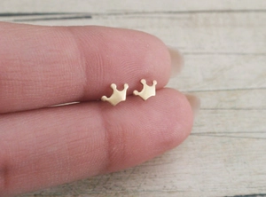 Macro shot of gold crown stud earrings on fingers showing the tiny minimalist size
