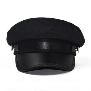 Close-up of black baker boy hat featuring a leather brim and gold metal button details