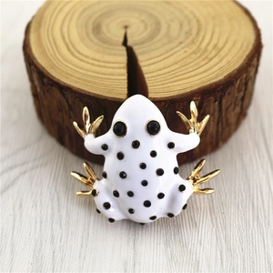 Macro shot of white enamel frog brooch with black dots and golden plated legs on wood