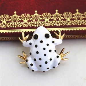 Detailed macro view of white enamel frog brooch with black dots and golden legs