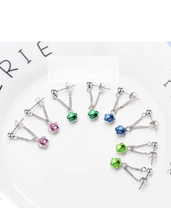 Macro shot of colorful floral crystal earrings in pink, green, and blue on white porcelain