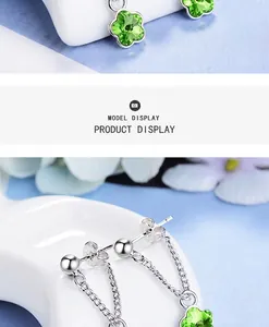 Détail de boucles d'oreilles argentées avec trèfle en cristal vert et chaîne fine