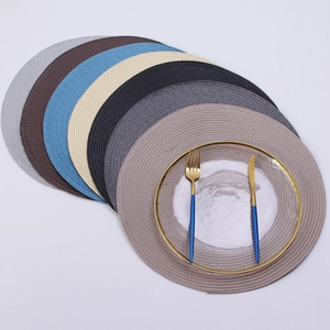 Set of round woven placemats in seven colors with elegant plate and golden cutlery setup