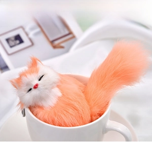 Detail of plush orange fox pendant sleeping in a ceramic cup with soft lighting