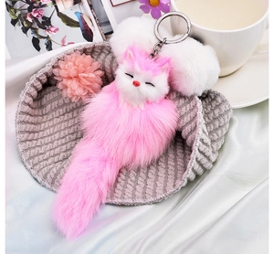 Close-up of pink plush fox keychain with long fluffy tail nestled in a knitted hat