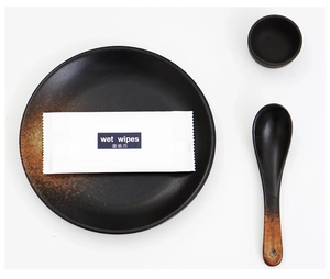 Flat lay of individual wet wipes package on minimalist black ceramic dinnerware
