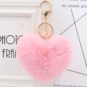 Detail of soft pink faux fur heart keychain with gold metal clasp on a white frame