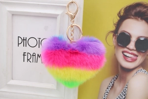 Rainbow heart-shaped plush keychain with golden metal clasp on decorative white frame