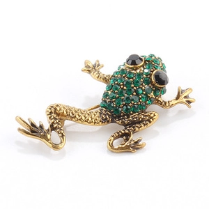 Detailed close-up of a golden frog brooch featuring vibrant green rhinestones and black gem eyes