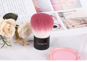 Détail du pinceau à poudre rose dégradé avec manche noir à côté du poudrier rose