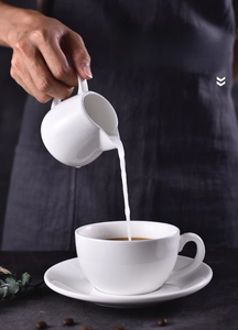 Close-up of textured white ceramic pitcher pouring milk for coffee latte art