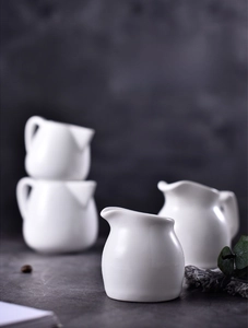 Close-up of four white ceramic creamers with handles and glossy glaze on a dark background