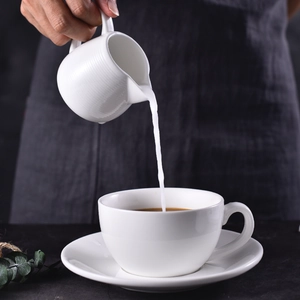 White ceramic coffee set with handled milk pitcher pouring milk into a cup
