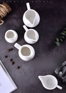 Detailed view of white ceramic creamers with handles and pouring spouts on stone background