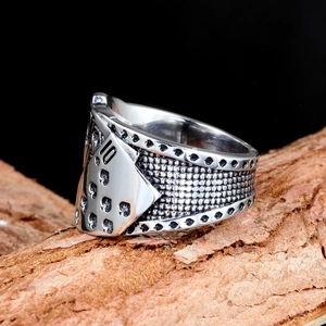 Close-up of vintage stainless steel spade 10 poker ring on a rustic bark surface