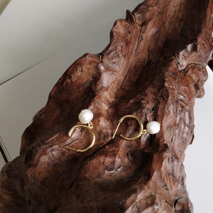 Detail of gold pearl hoop earrings on a rustic wood block highlighting the texture