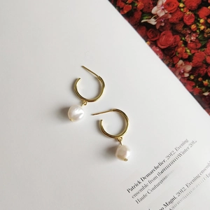 Detail of elegant gold C-shape earrings with natural baroque pearls on a magazine backdrop