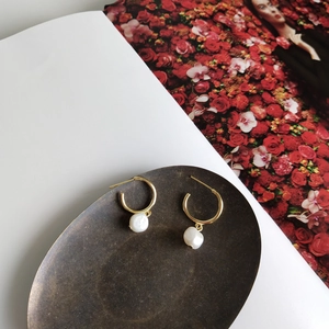 Detailed view of baroque pearl earrings with gold hoops on a vintage bronze tray