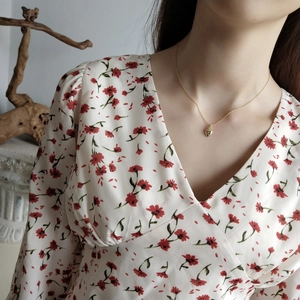 Detail of a dainty gold heart pendant necklace worn with a floral V-neck dress