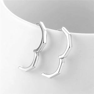Minimalist silver geometric hexagonal hoop earrings displayed on white ceramic rim