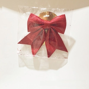 Close-up of a festive red glitter Christmas bow ornament in clear retail packaging