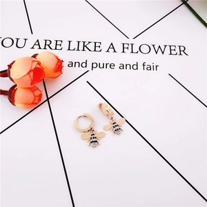 Détail de boucles d'oreilles créoles dorées avec pendentif abeille et cristaux incrustés