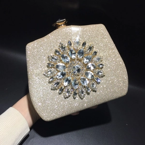 Detail of gold evening clutch featuring a large sunflower rhinestone buckle on sparkling fabric