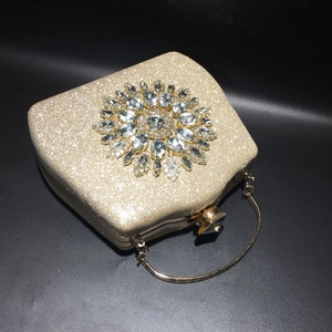 Detail of gold glitter evening bag featuring a rhinestone sunflower and metal ring handle