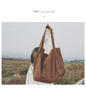 Detailed view of brown canvas tote bag with shoulder strap held against a field background