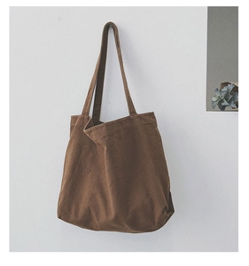 Detail view of large brown canvas tote bag hanging against a minimalist white wall