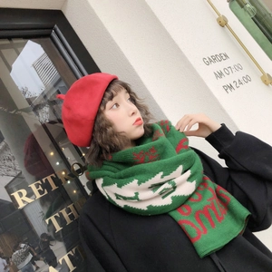 Detail of green knitted Christmas scarf featuring red reindeer and Xmas text patterns