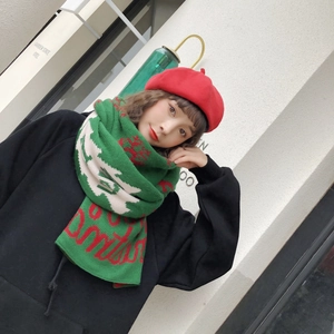 Close-up of a green knitted scarf featuring red and white Christmas reindeer patterns