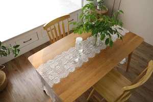 Macro detail of white eyelash lace table runner with floral patterns on wooden table