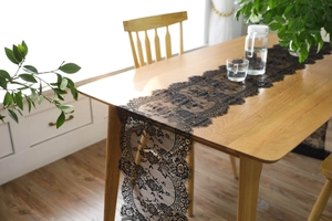 Detail of black eyelash lace table runner with floral patterns on a wooden table