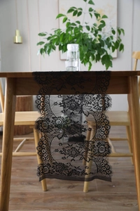 Detail of black eyelash lace table runner with floral patterns on a wooden table