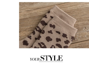 Close-up of leopard print knitted socks showing the ribbed cuff texture on a wooden surface