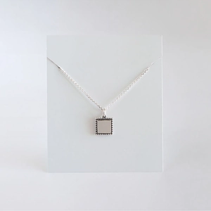 Macro shot of silver S925 square pendant necklace with intricate beaded edge details
