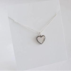 Macro detail of S925 sterling silver heart pendant with beaded edge on display card