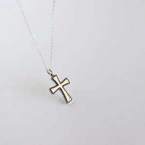 Close-up of a minimalist S925 sterling silver cross pendant necklace on a grey background